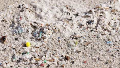 close-up of microplastics and debris scattered on sandy beach in daylight