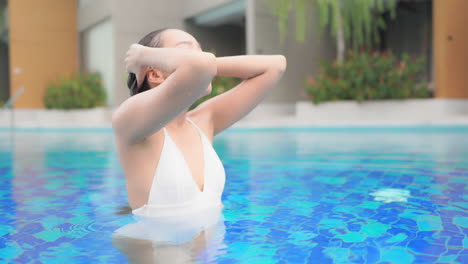 A-beautiful-woman-in-a-white-one-piece-bathing-suit-smoothes-her-wet-hair-back-away-from-her-face-as-she-emerges-from-the-pool