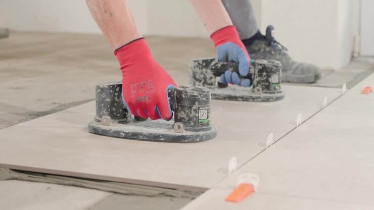 Placing a huge tile on the floor by a professional tiler using vacuum holders.