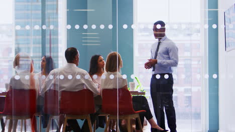 Young-male-boss-stands-addressing-business-team-at-meeting