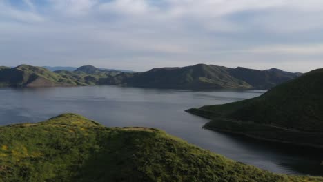 Drone-wide-shot-of-California-mountain-top-covered-in-yellow-wildflowers-during-the-superbloom-with-large-lake-in-background