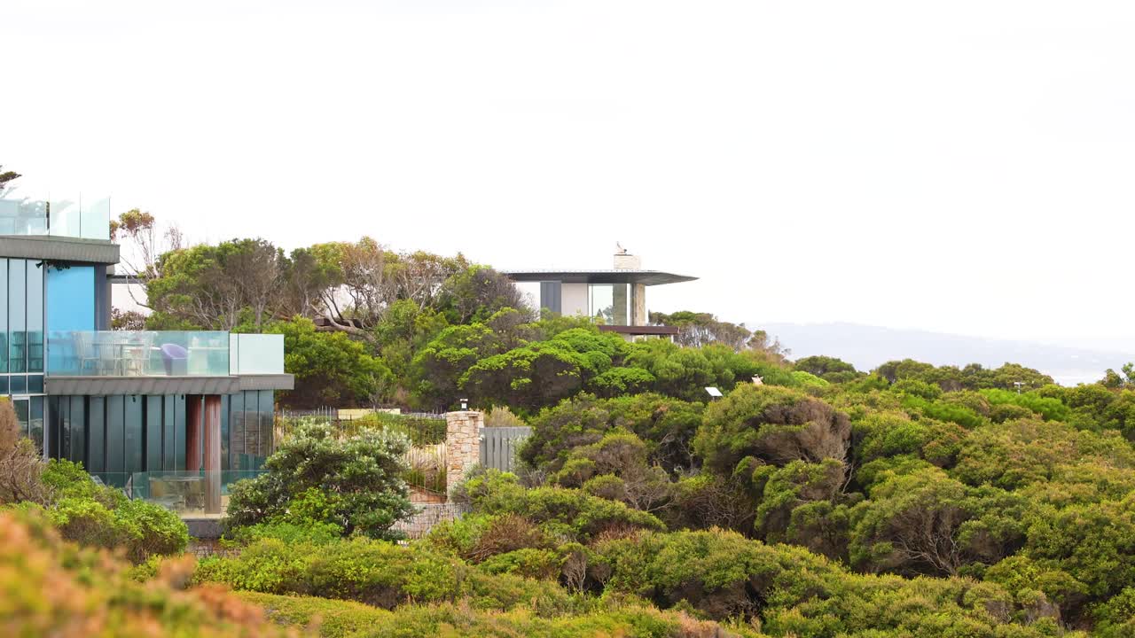 A modern glass building nestled in vibrant greenery along Australia's Aireys Inlet, captured in bright daylight