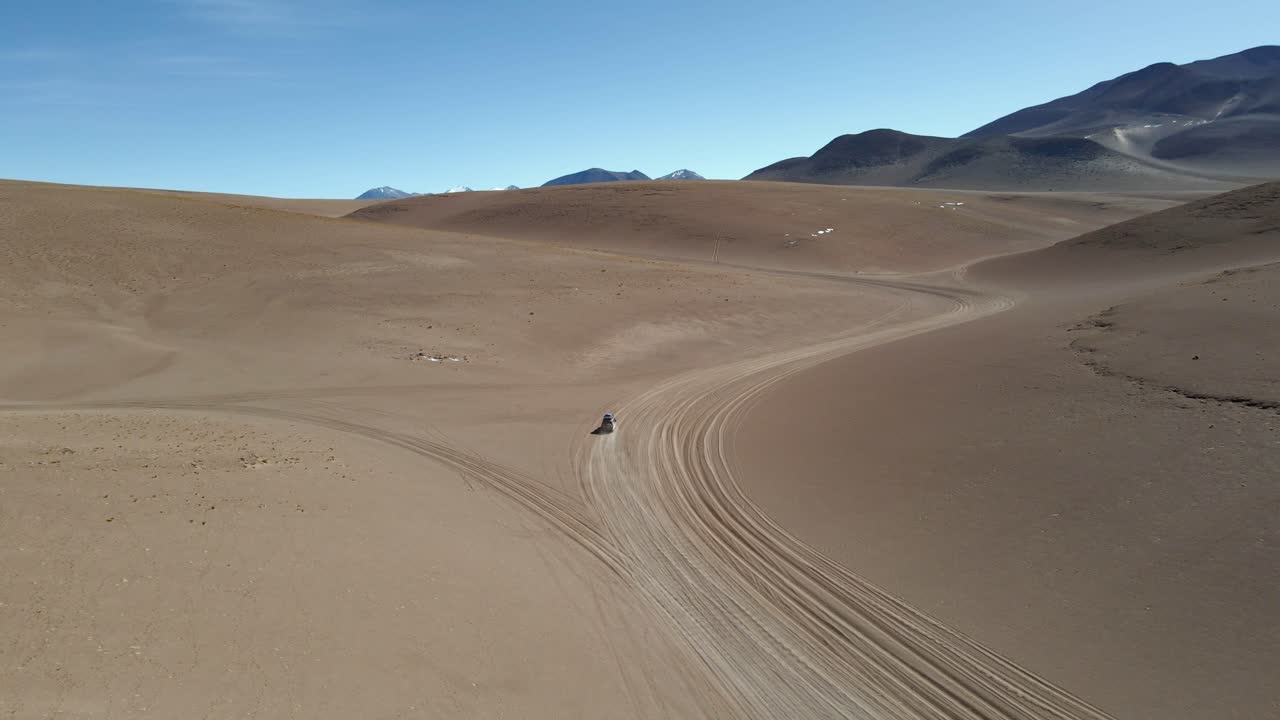 Drone glides over Bolivia desert dunes with soft light illuminating tracks and distant hills