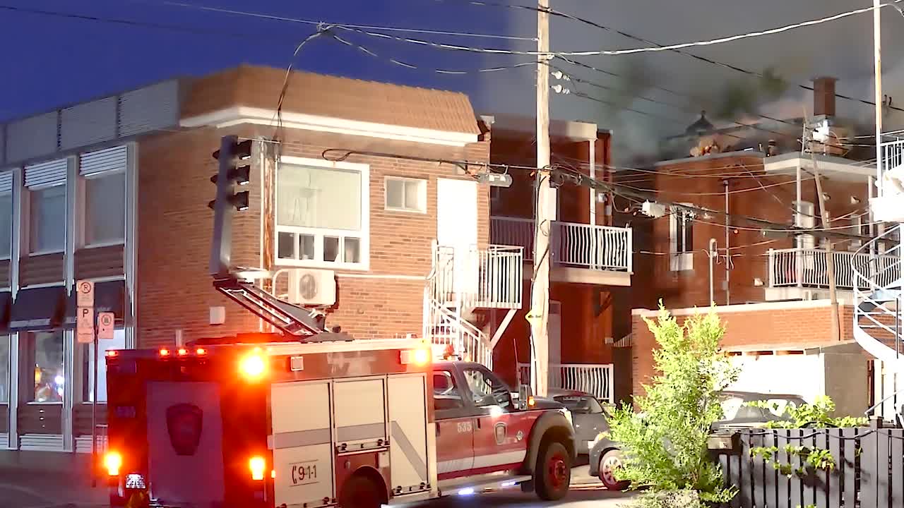 Firetruck moving lights to building as firefighters work during night on street in Montreal, Quebec.