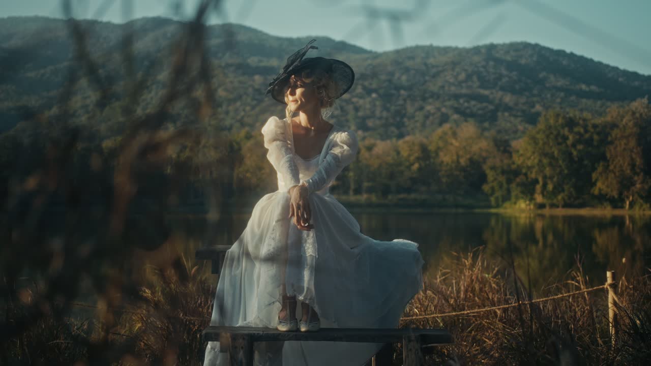Donna elegante in abito vintage seduta vicino a un lago sereno con montagne