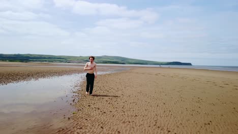 orbital footage of a young man without a shirt walking alone on a beach