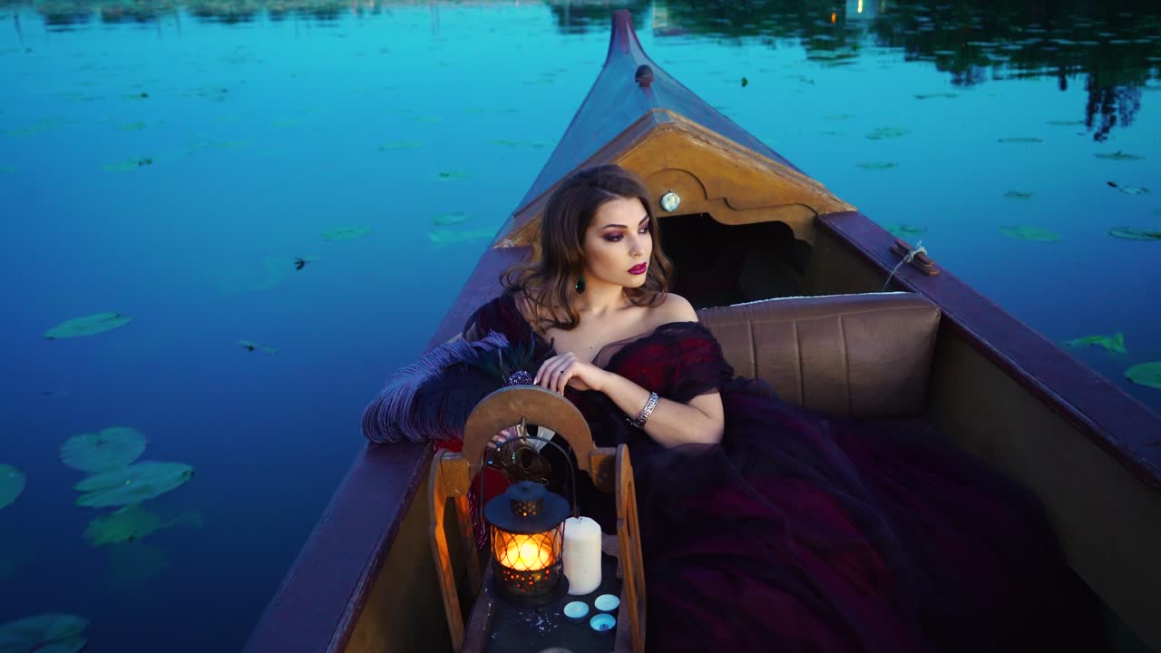 Beautiful woman enjoys the evening nature while traveling by boat at sunset. Portrait of a dreamy female relaxing at sunset sailing alone in gondola