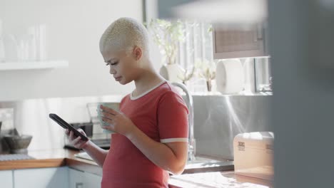 mujer biracial feliz bebiendo café y usando un teléfono inteligente en casa en cámara lenta
