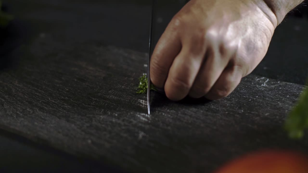 Close-up of a Chef's Hands Chopping Fresh Herbs on a Slate Cutting Board