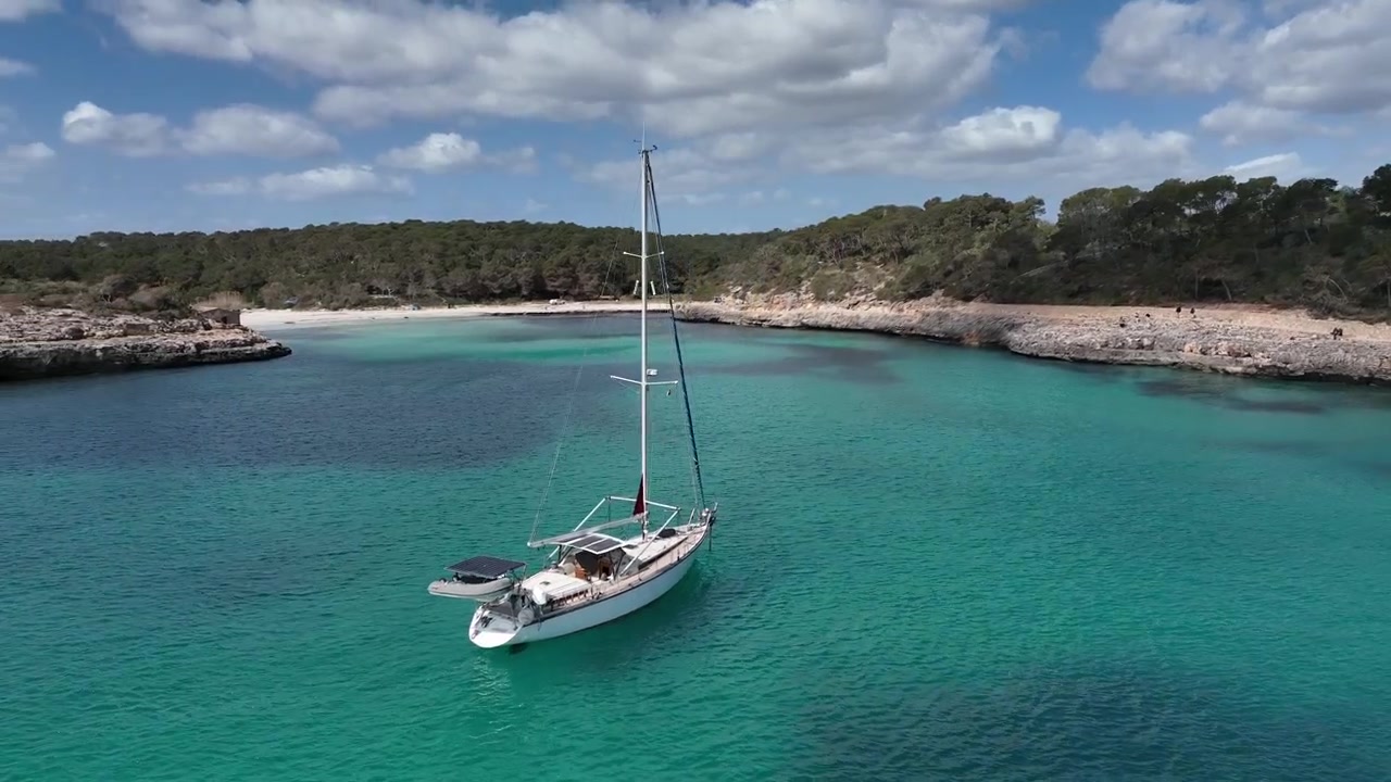 Ripresa aerea con drone di una barca a vela ancorata in acque limpide e turchesi all'interno di una baia riparata dell'Algarve, circondata da aspre scogliere rocciose e fitta vegetazione costiera in Portogallo.