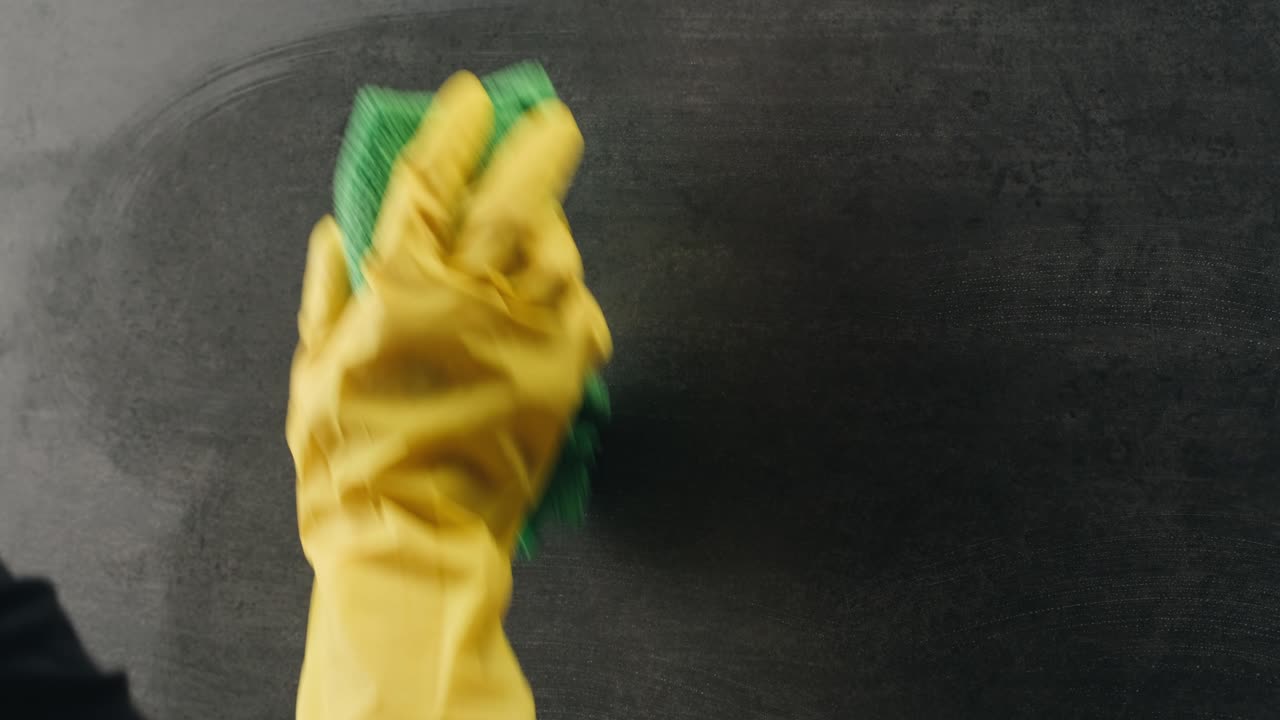Close-up de uma mão com luva amarela limpando uma superfície escura