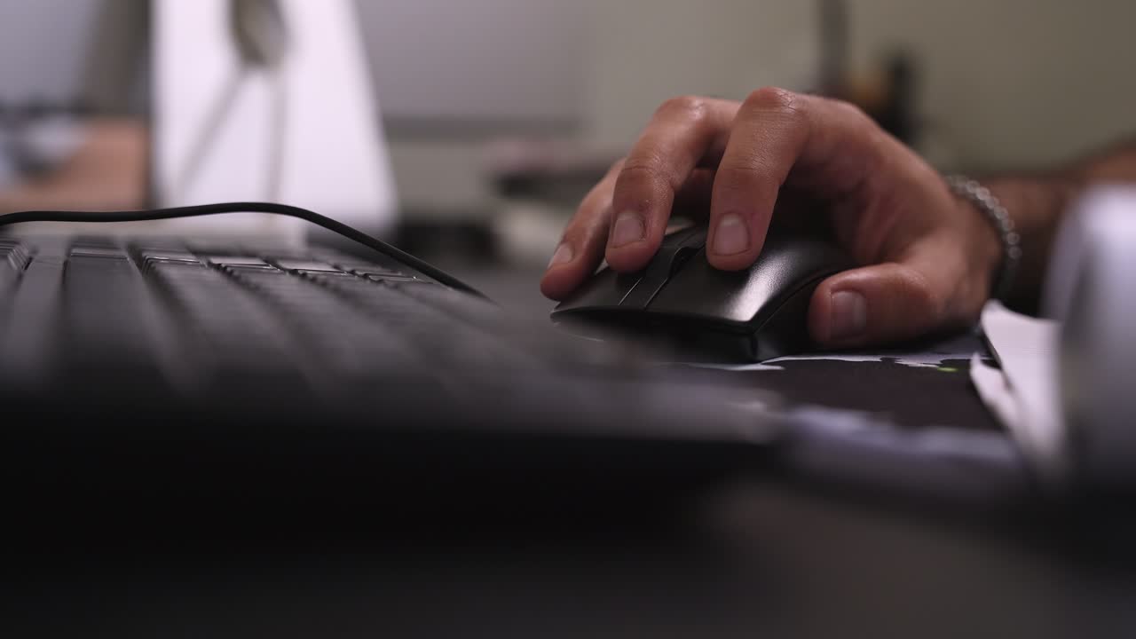 a hand typing on a keyboard at a modern office desk beside a computer mouse, captured indoors with soft light and shallow depth of field