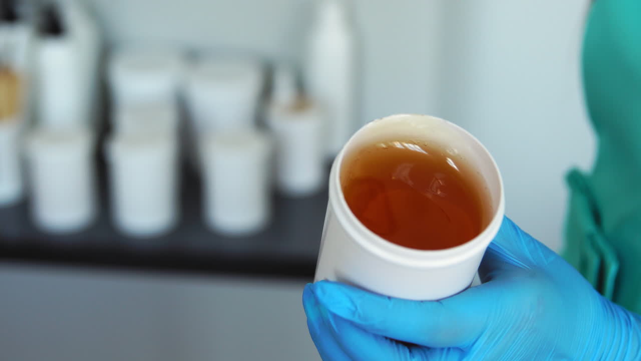 Primo piano di mani con guanti di gomma che aprono un barattolo di zucchero per la depilazione con il sugaring.
