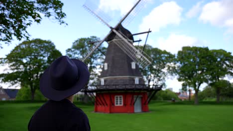 man wearing a hat looking at a traditional danish windmill in kastellet