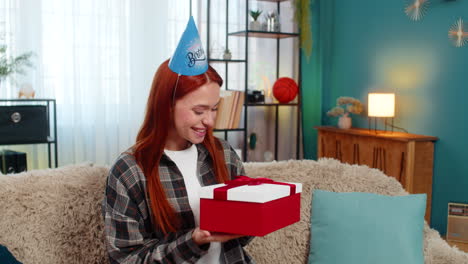 woman wearing party hat opening birthday gift looking pleasantly surprised and emotional happy