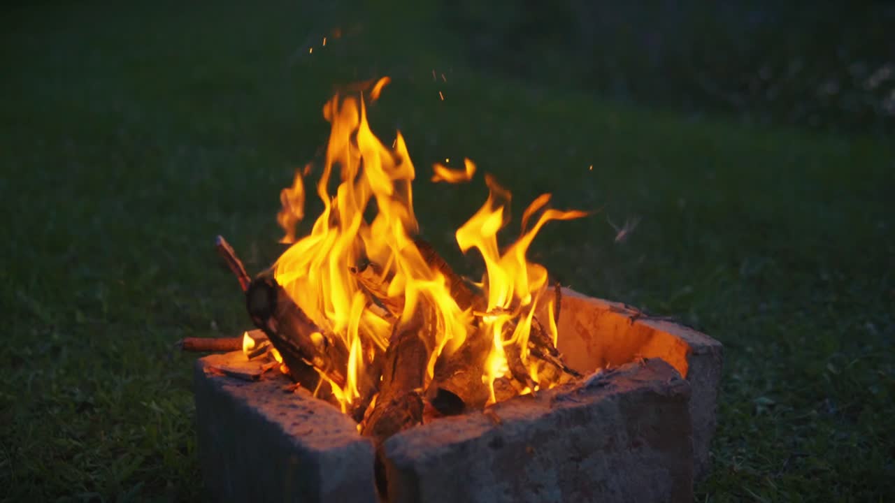 Primo piano di fiamme vivaci di un falò che bruciano legna all'interno di un focolare sull'erba, catturando calore, energia e l'atmosfera del campeggio all'aperto di notte a Savci, Slovenia