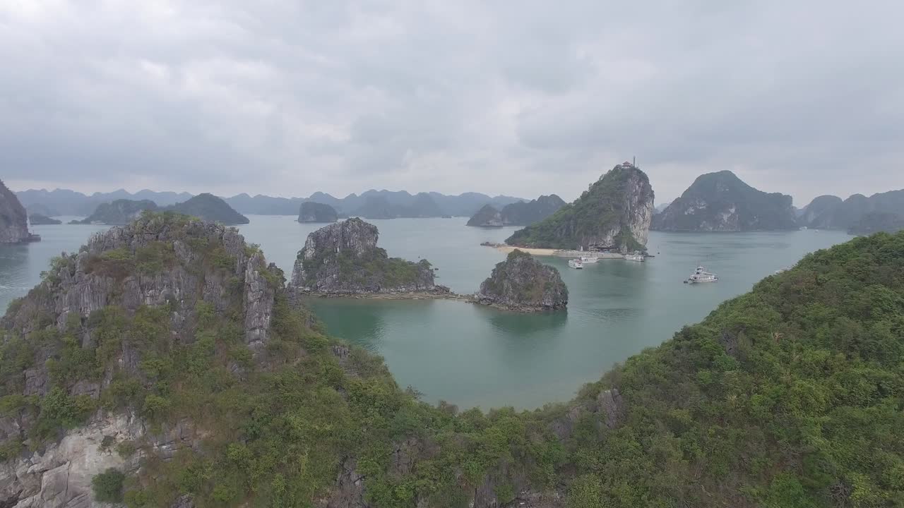 Aerial drone footage of Ha Long Bay showcasing limestone islets, calm turquoise waters, and lush greenery under cloudy skies, highlighting natural beauty and tranquil seascape