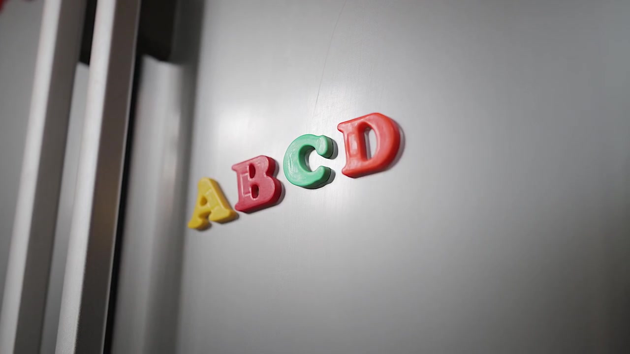 クローズアップ：子供の手がキッチン冷蔵庫にマグネットのアルファベット文字を置く。