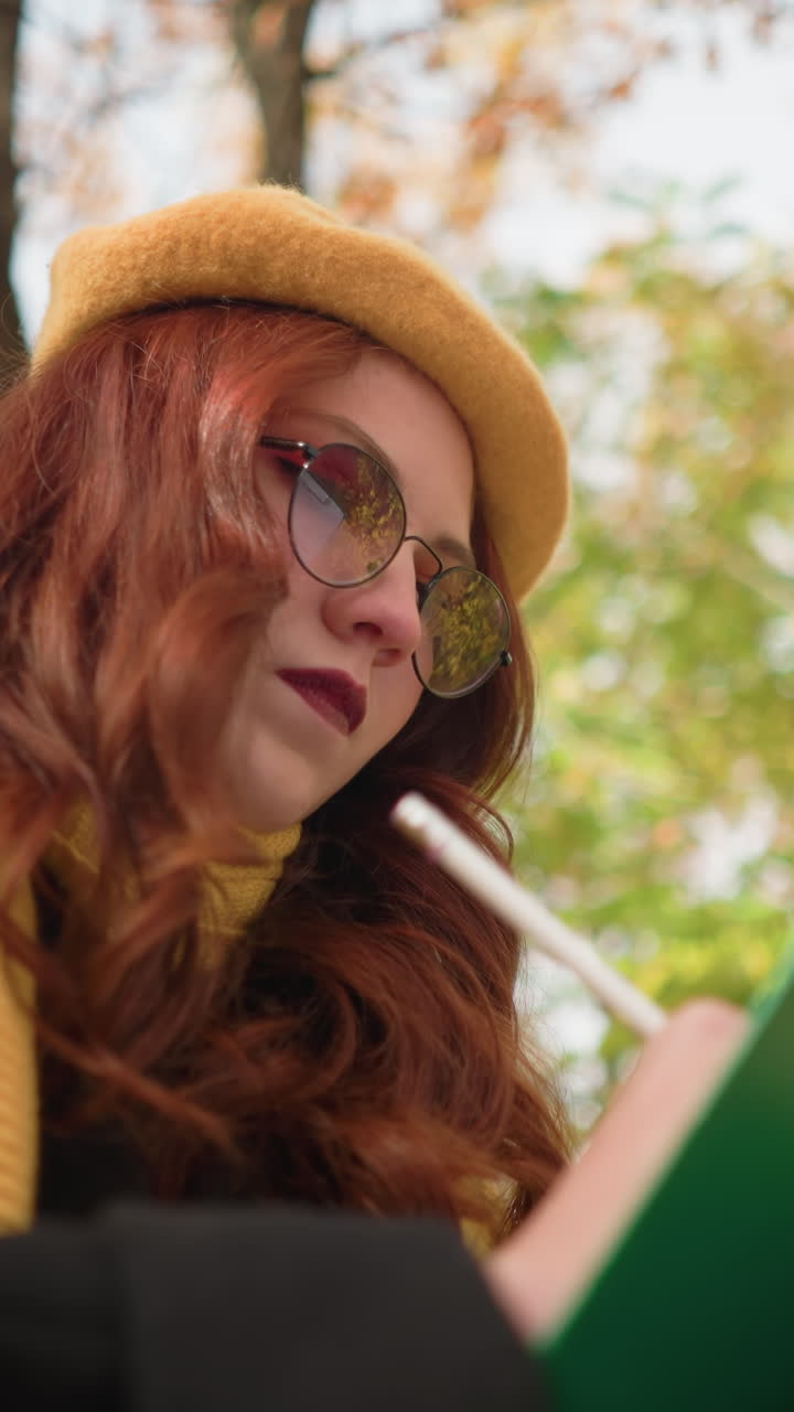 vista de ángulo inferior de la mente talentosa dibujando pensativamente en el lienzo, sentada con la cabeza inclinada. inmersa en el enfoque artístico, con una elegante boina amarilla y bufanda, rodeada de cálidos colores de otoño