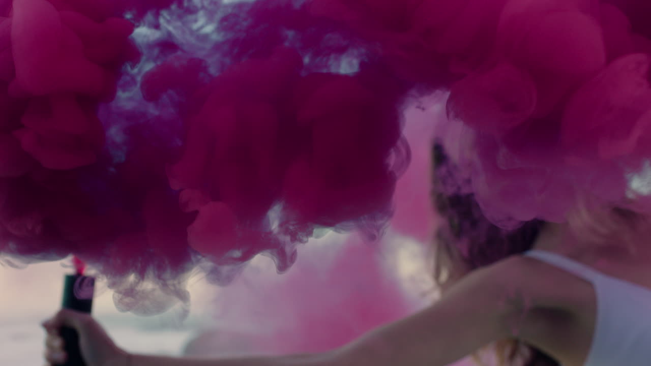 donna che tiene in mano una granata di fumo rosa che balla sulla spiaggia all'alba celebrando la libertà creativa