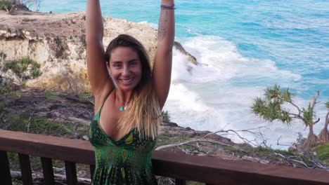 happy woman raising both hands with crashing waves in background - north gorge walk in point lookout, qld, australia