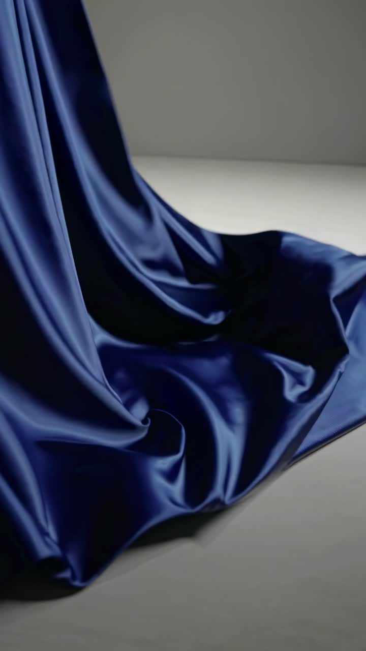Un fotogramma video di un elegante tessuto di seta blu drappeggiato in modo uniforme, catturato da una angolazione bassa