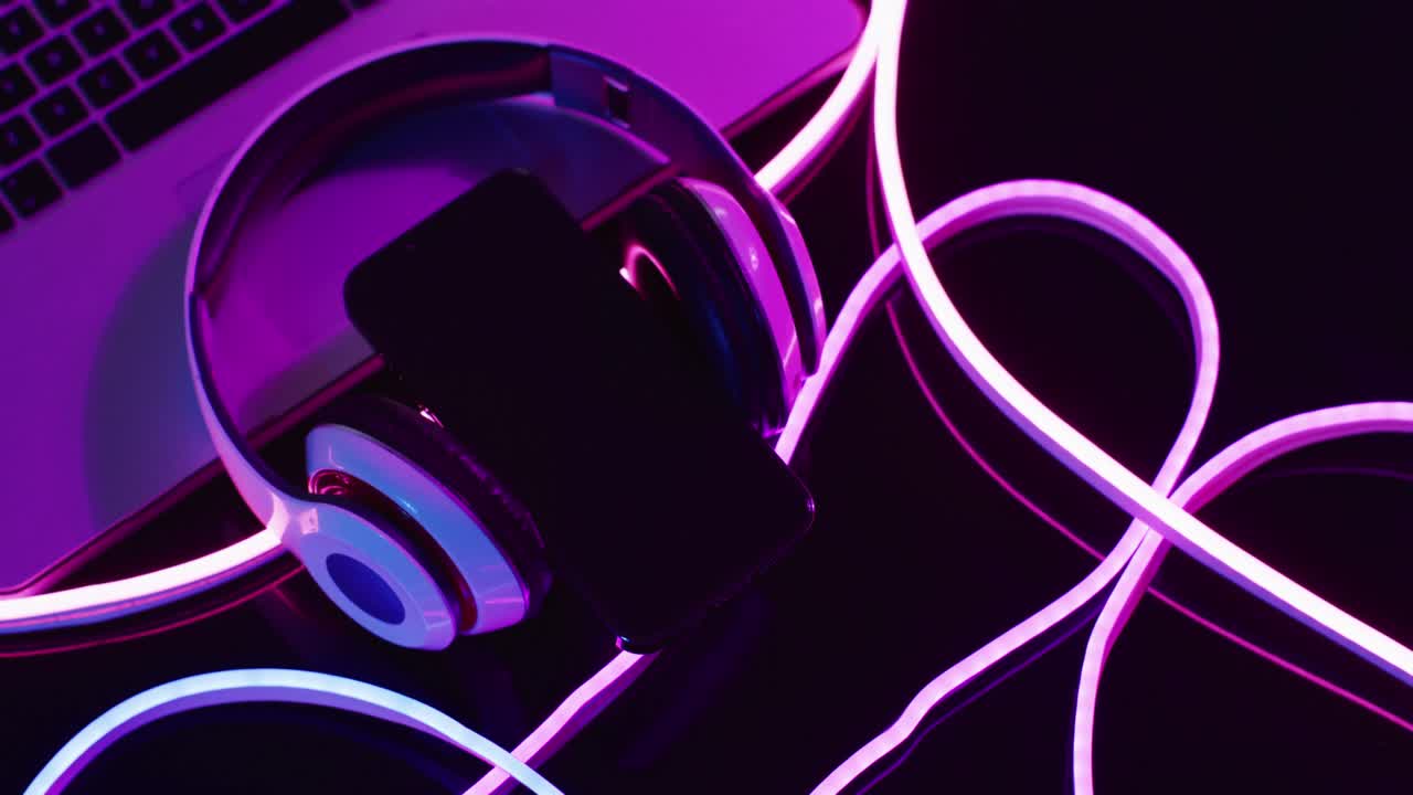 Komposition af bærbar computer, hovedtelefoner og smartphone med lyserøde neonlys på sort baggrund.