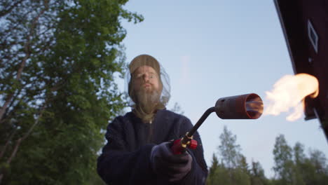 eccentric man with crazy eyes wearing mosquito head net waves around blowtorch