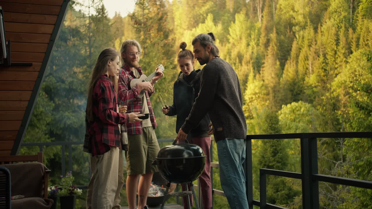 A group of friends cook food on the grill and listen to the guitar at a barbecue picnic in a country house overlooking the forest and mountains