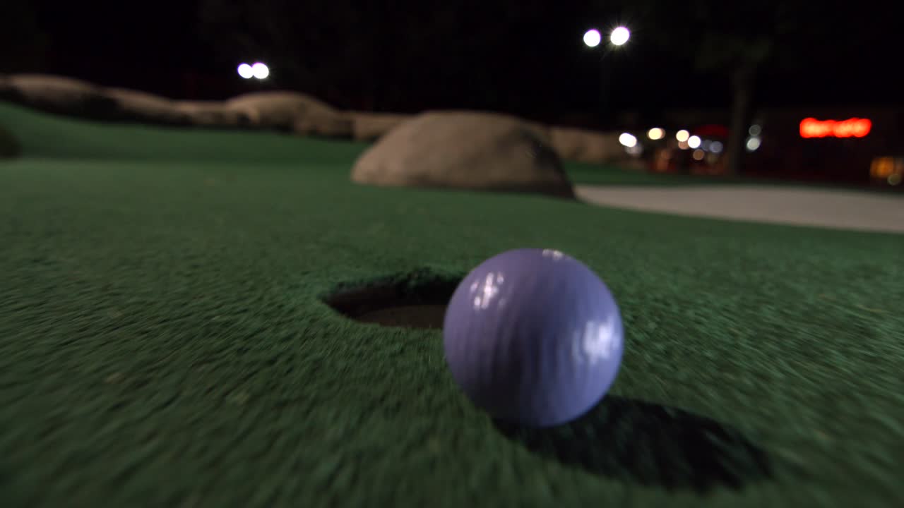 una mini pelota de golf morada cae en el hoyo de golf y rebota en el bolsillo de un campo