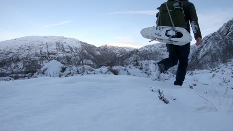 tired snowboarder walking uphill with snowshoes on back - hardangervidda norway europe