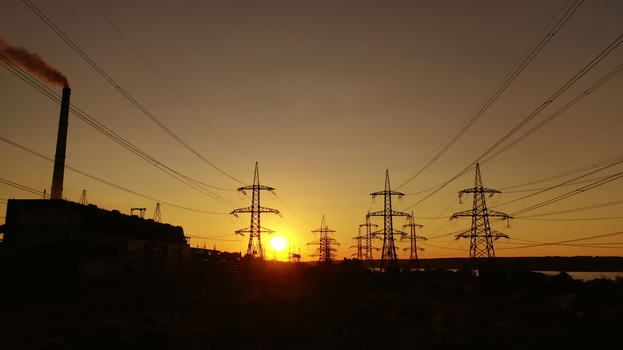 Electric power station in the evening. High voltage electric lines against the setting sun. Transmission lines. Motion camera back.