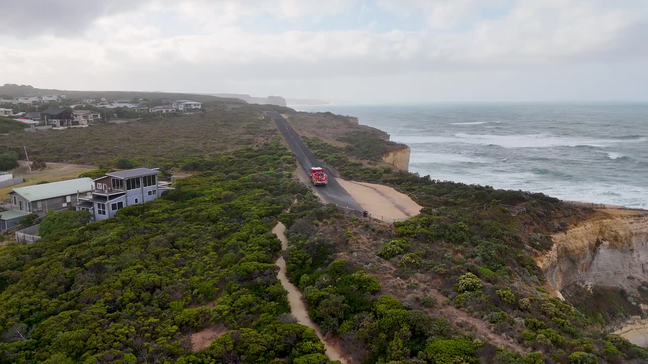 Aerial view of a fire engine traveling along a scenic coastal road in Port Campbell, Australia, highlighting road erosion and ocean views
