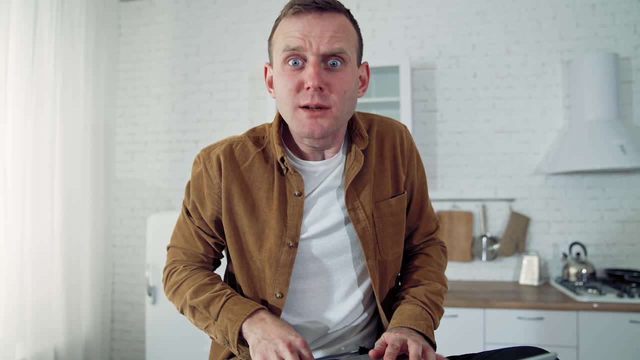 Nervous businessman during quarantine. Young man freelancer with a laptop sitting on a table in the kitchen and typing angrily. Work at home during lockdown.