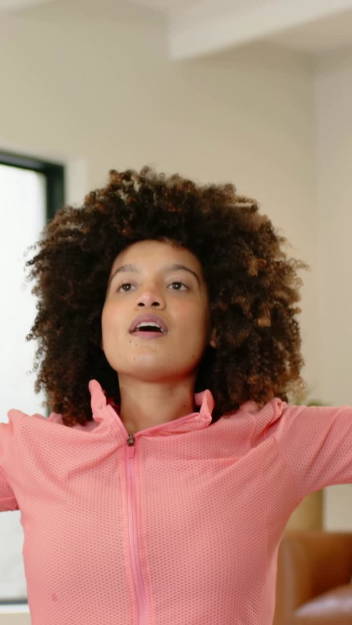 Vertical video: Kneeling woman in pink jacket stretching and reaching up on mat at home with watch