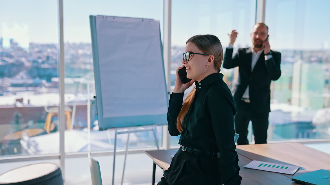 Business people talking on their phones indoors. Smiling woman having a conversation through the phone in modern office. Businessman near the window with city background.