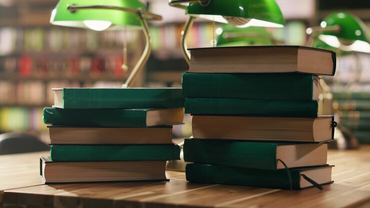 Pila de libros de tapa dura verdes en un escritorio de biblioteca con estanterías borrosas