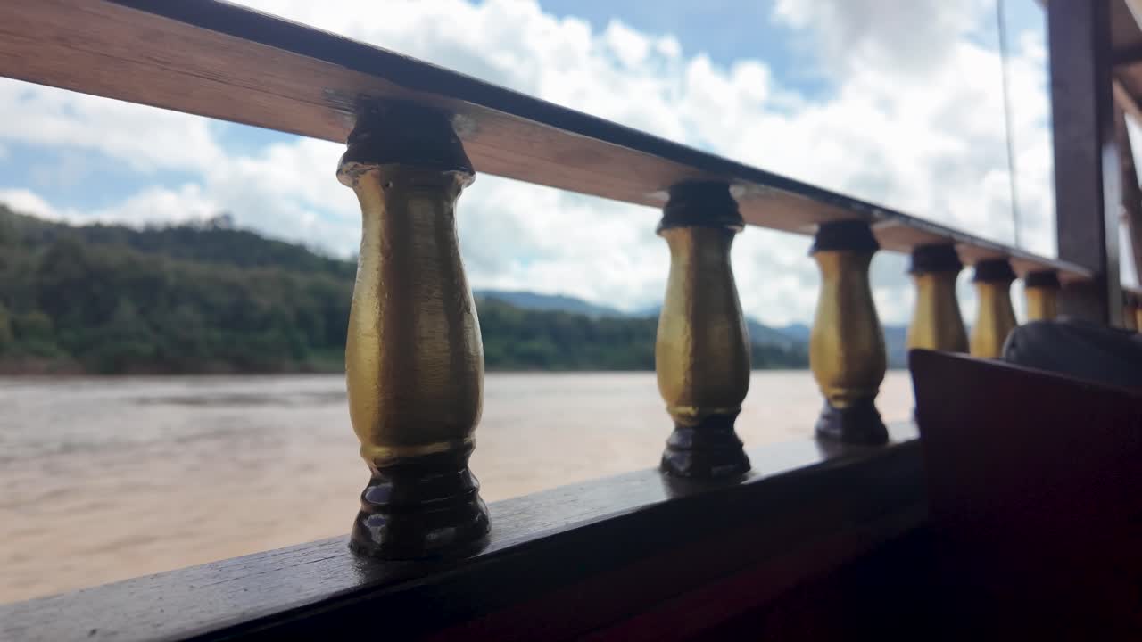 View of the Mekong River from a slow boat with wooden railing details in Laos Southeast Asia