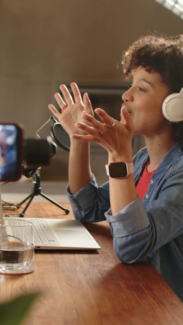 Video vertical: Grabando con el teléfono, un anfitrión vestido de mezclilla habla y ajusta los teléfonos en casa, con un micrófono de podcast.