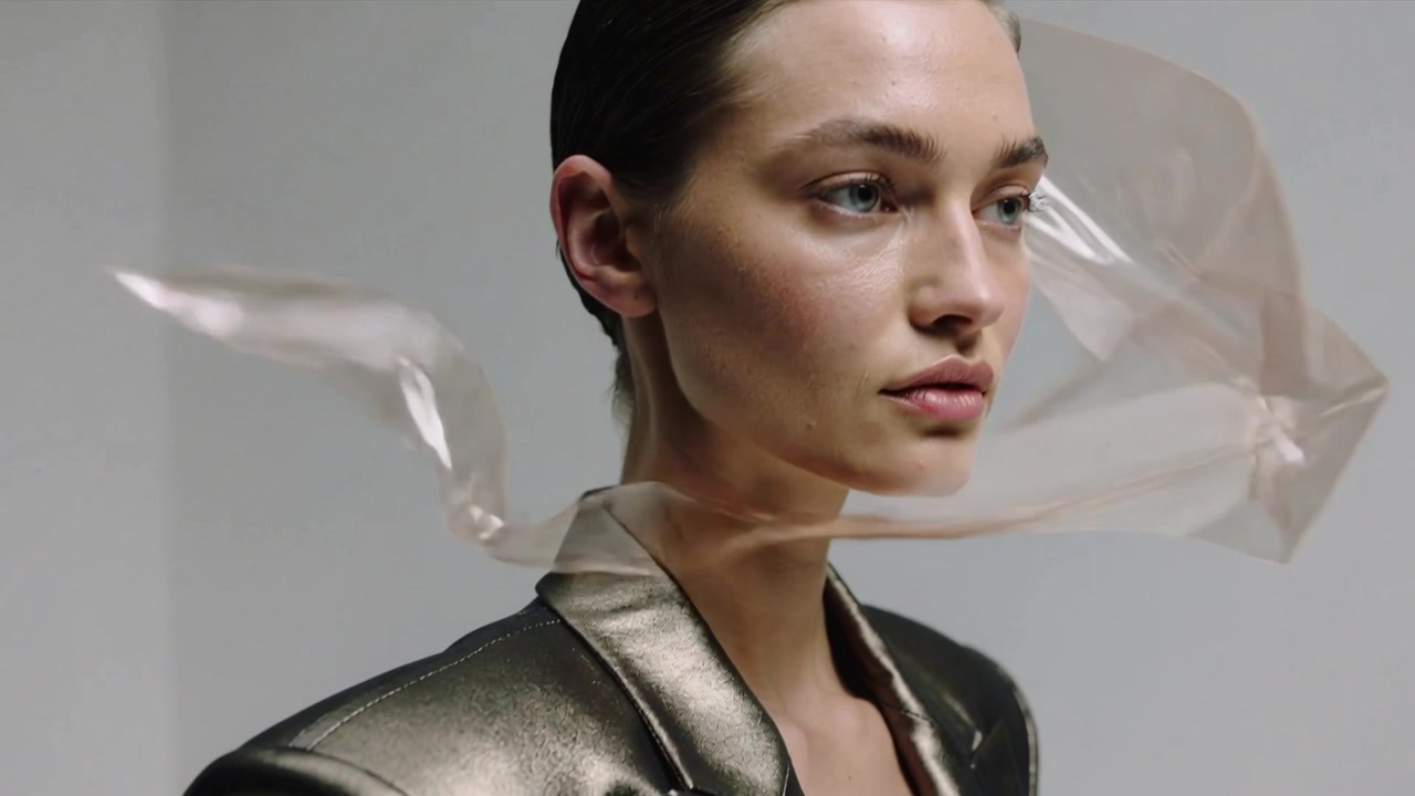 Sweeping plastic sheet forming veil, female model posing in studio, revealing face, metallic blazer