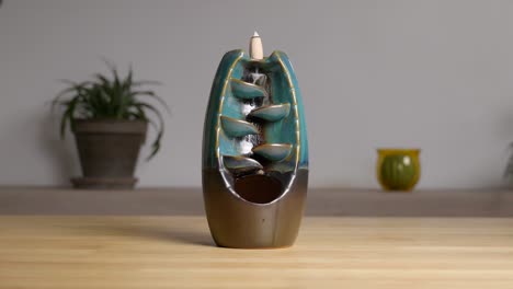 ceramic backflow incense holder creating aromatic smoke cascade on wooden table