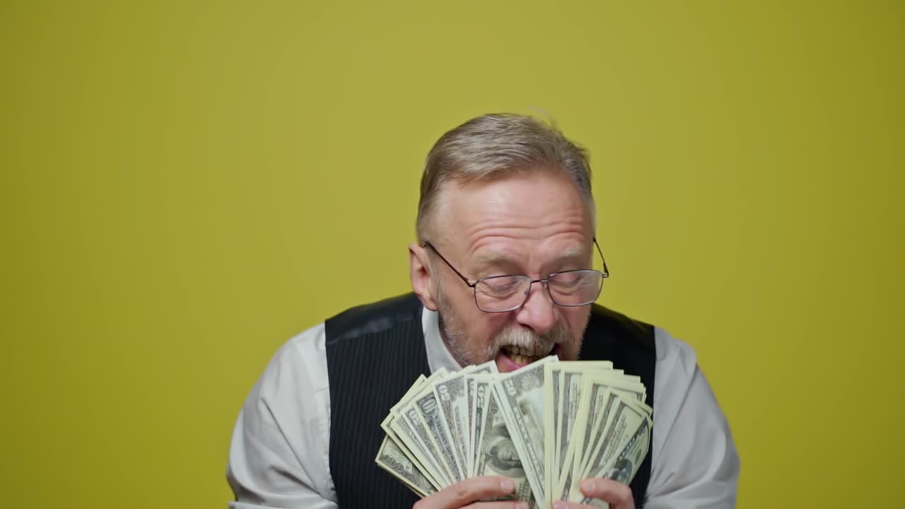Happy old man with dollars in his hands. Positive rich man demonstrates his money. Face of a funny senior man with money. Close-up.