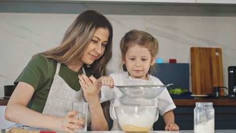 la madre ayuda a la hija a tamizar la harina con el tamiz cocinando juntos