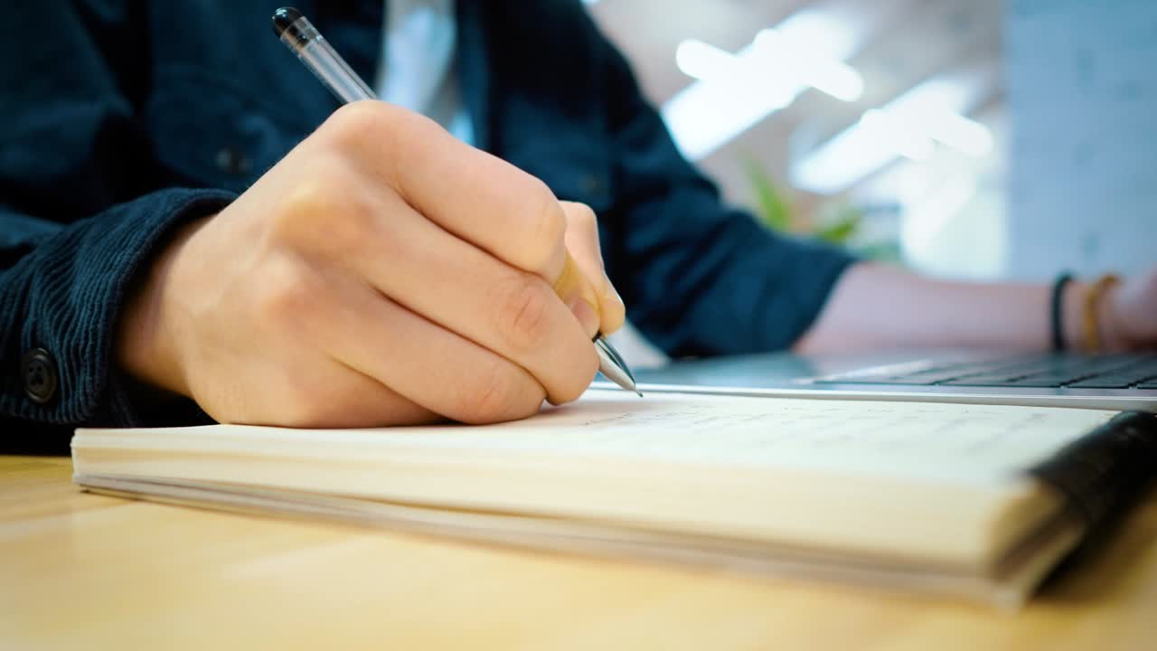 한 남자가 한 손으로 노트북에 메모를 쓰고 다른 손으로 노트를 입력합니다.