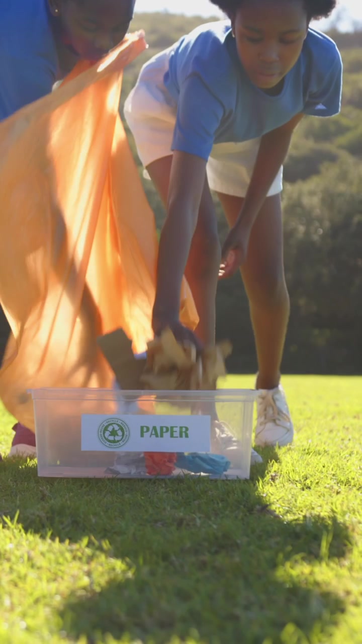 Girls approaching PAPER bin carrying orange bag, emptying colorful recyclables for school cleanup