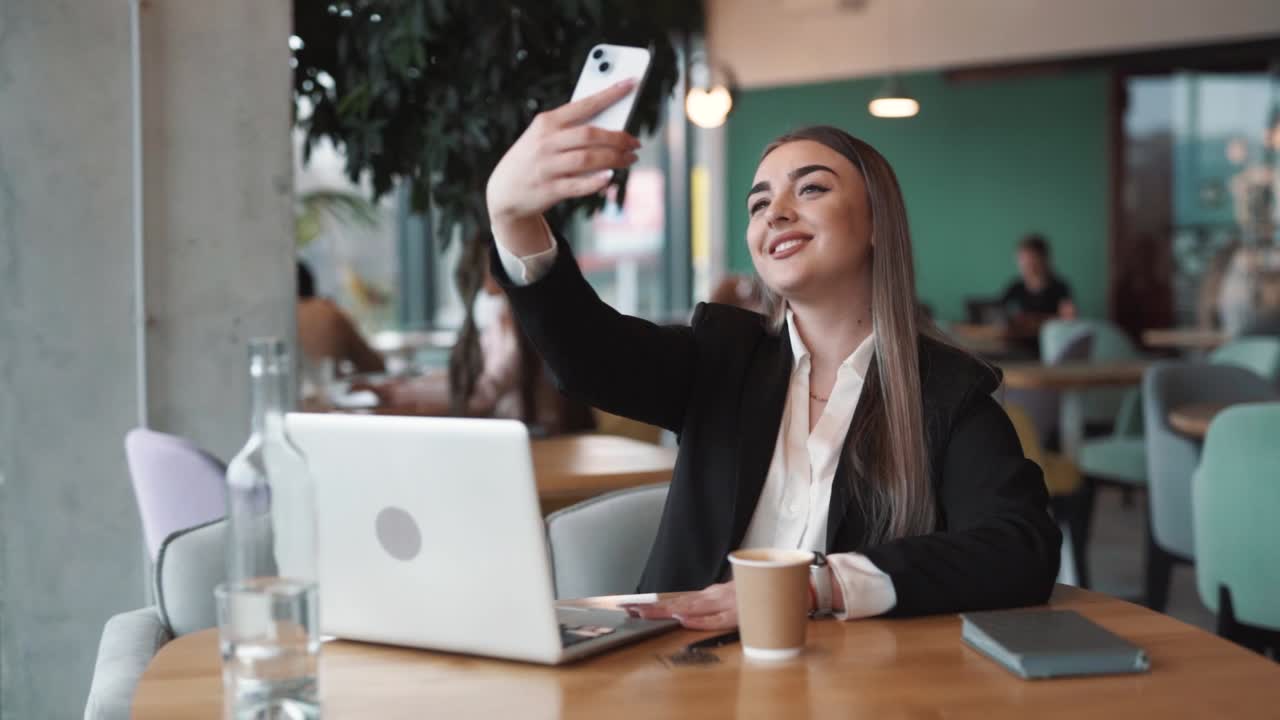 una mujer hermosa sentada en un café con ropa de negocios toma una selfie con una sonrisa en su cara en un teléfono inteligente