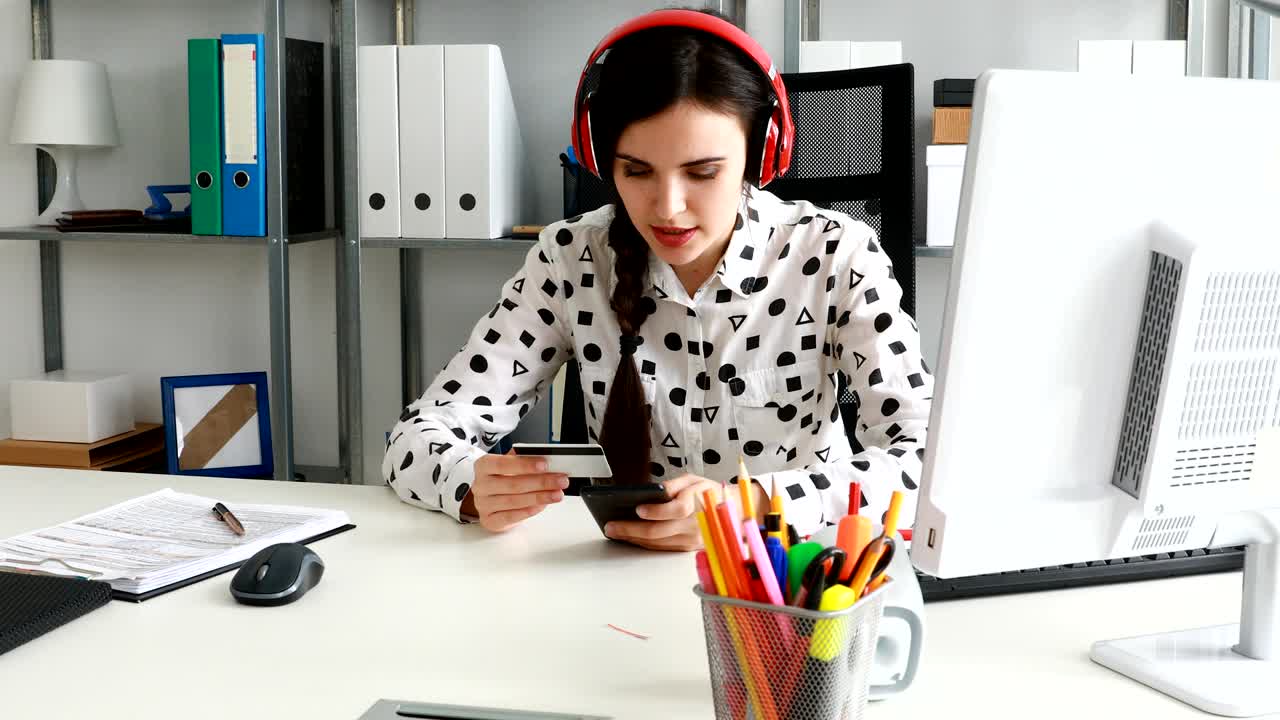mujer de negocios con auriculares rojos ingresando el número de tarjeta de crédito en el teléfono inteligente