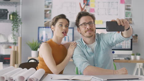arquitectos masculinos y femeninos en la oficina posando para selfies y haciendo caras divertidas juntos