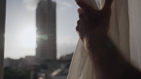 Hands open the curtain on the window. Sun rays shine through. Urban city in the background view. Man opening window blinds. tall building blurred. morning routine. new starts. lens flare