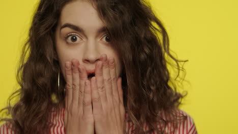 shocked woman open mouth. shock girl closing mouth with hands in yellow studio